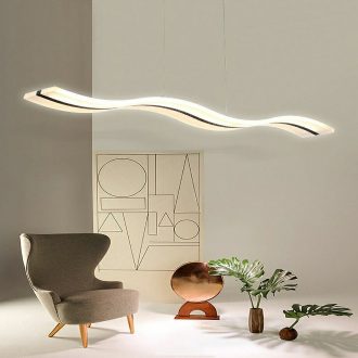 Modern wave-shaped pendant light above an armchair and decorative items in a chic room.