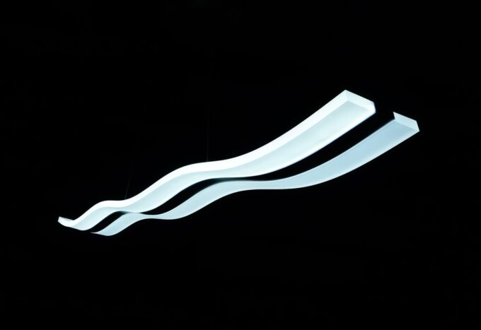 Modern wave-shaped LED pendant light on a dark background.