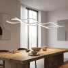 48aa5c00-9217-4511-9974-bd3e81b195d7 Modern dining room with a wave-shaped chandelier above a wooden table set for four, featuring ceramic dishes.