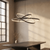 254c4b53-34dc-43dd-a4b0-87f87da2502a Modern dining room with geometric pendant light, wooden table, vase with branches, and sunlight through large window.