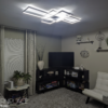 IMG20230306190128 Modern living room with geometric ceiling light, white leather chair, shelves, TV, plants, and beige decor.