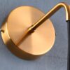 2 Gold wall-mounted lamp with a black cord against a grey background.