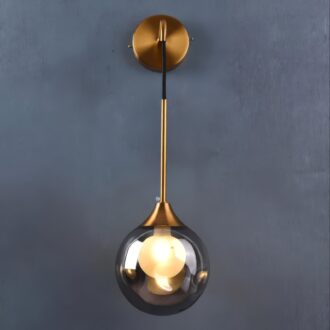 Modern gold pendant light with a clear globe against a gray wall.