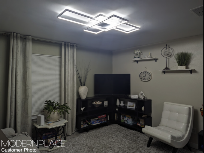 IMG20230306190128 Modern living room with geometric ceiling light, white leather chair, shelves, TV, plants, and beige decor.