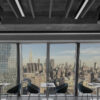 window-highrise-LED-installation Modern office with large windows offering a panoramic view of the city skyline, featuring stylish seating and tables.