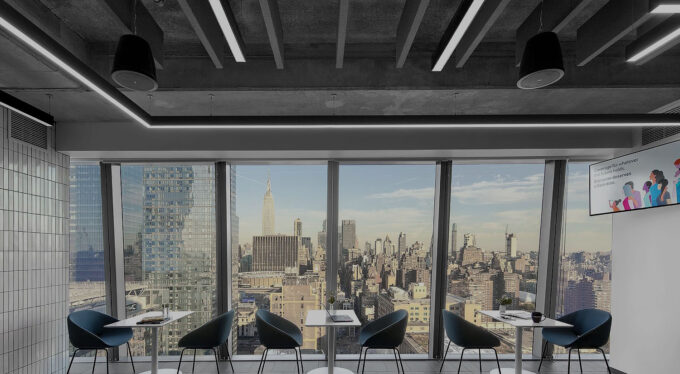 window-highrise-LED-installation Modern office with large windows offering a panoramic view of the city skyline, featuring stylish seating and tables.
