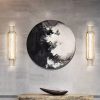 Round abstract wall art between two vertical wall sconces above console table.