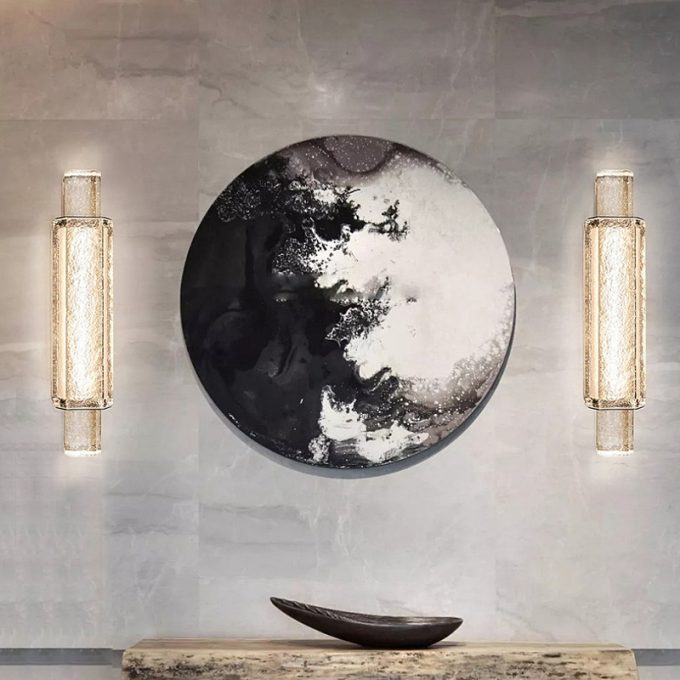 Round abstract wall art between two vertical wall sconces above console table.
