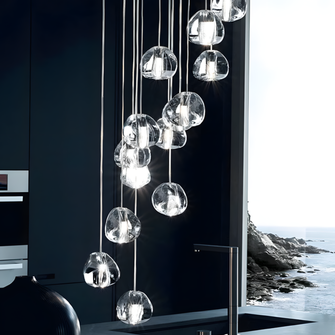 4 Modern pendant lights hanging in a dark kitchen with an ocean view through the window in the background.