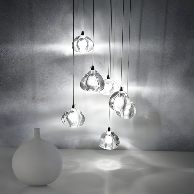 5 Modern glass pendant lights create artistic illumination against a textured wall with a minimalist white vase in the foreground.