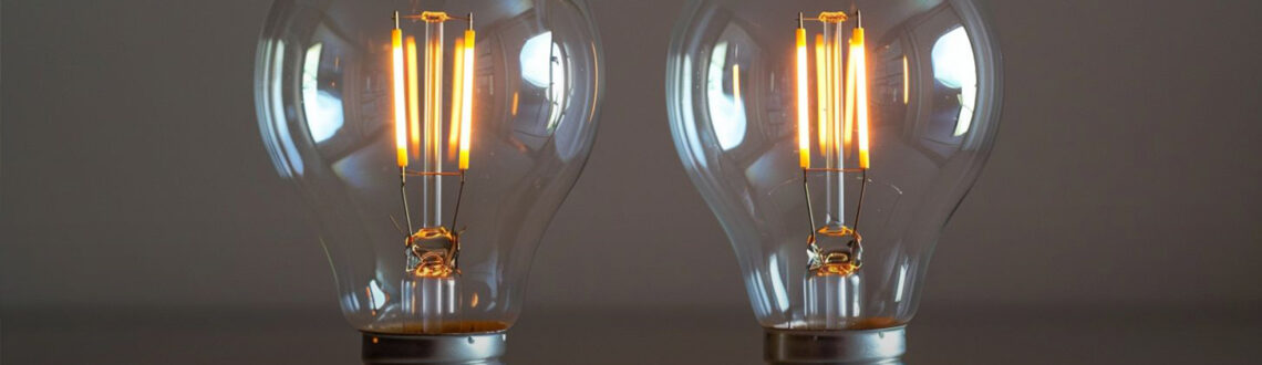 Close-up shot comparing E26 and E27 light bulbs with focus on screw lengths and voltage requirements.