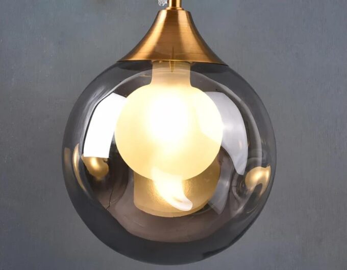 1 Modern suspended pendant light with illuminated bulb inside clear glass orb.
