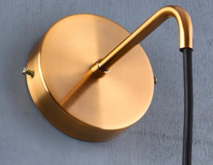 2 Gold wall-mounted lamp with a black cord against a grey background.