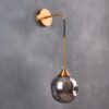 4 Modern gold wall-mounted sconce with a smoky glass globe on a gray background.
