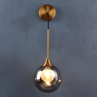Modern gold pendant light with a clear globe against a gray wall.